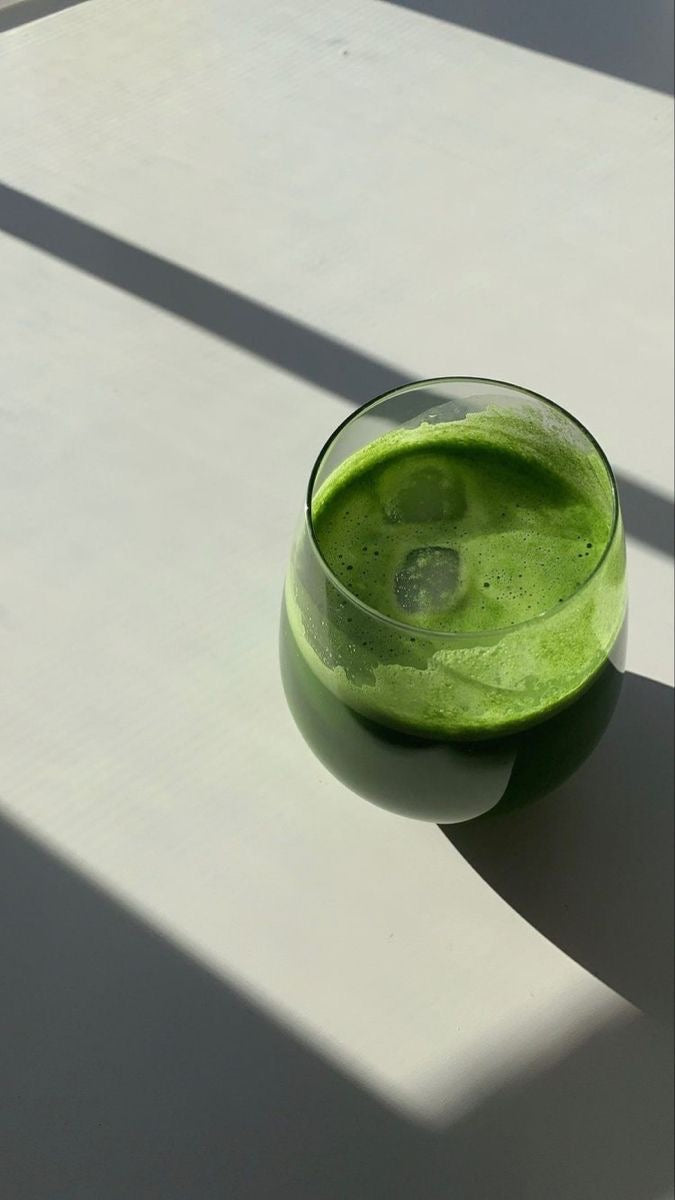 Close-up of a vibrant green drink with ice cubes in a clear glass, illuminated by natural sunlight, emphasising freshness and vitality