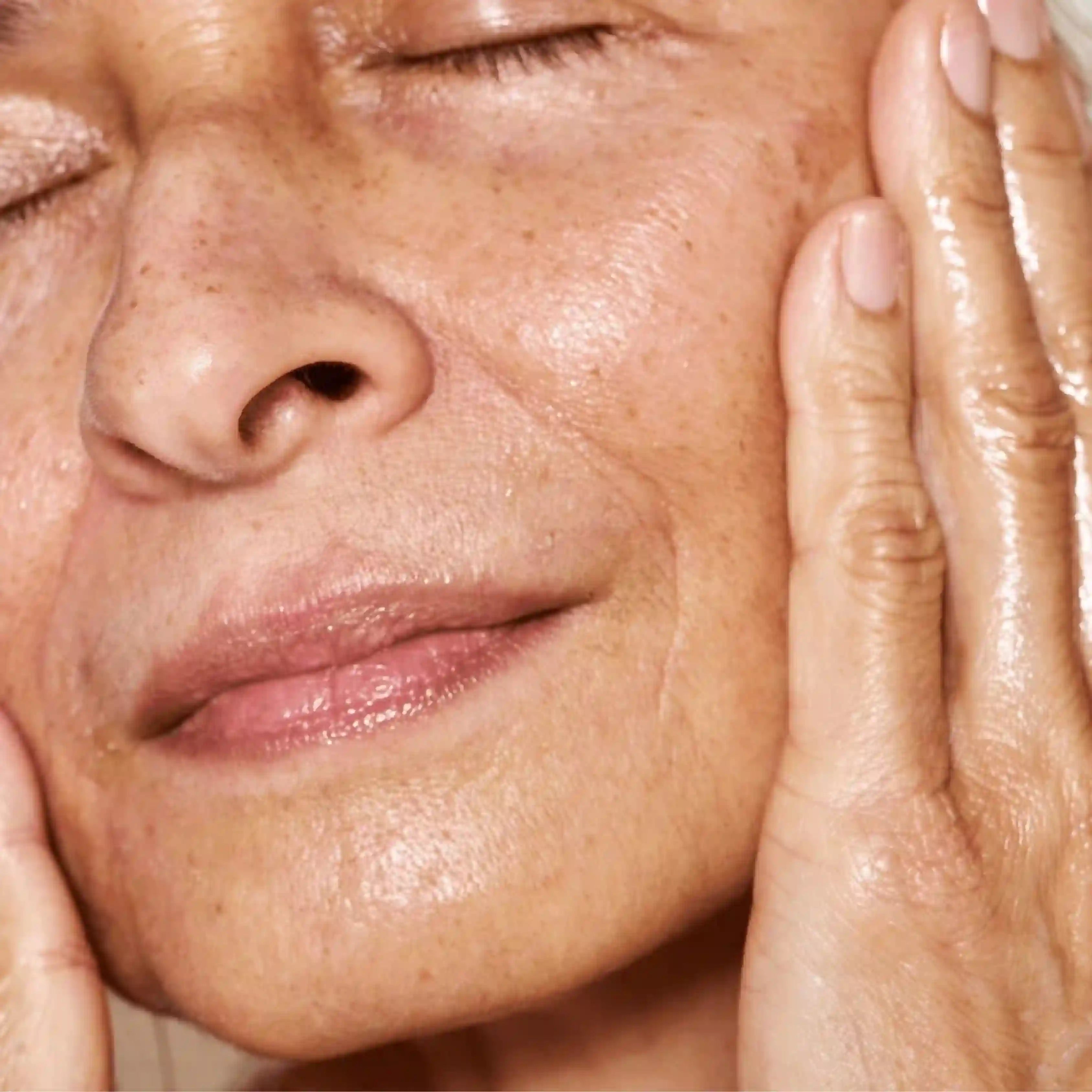 An older woman with fantastic skin smiling and holding her skin which is shiny and healthy