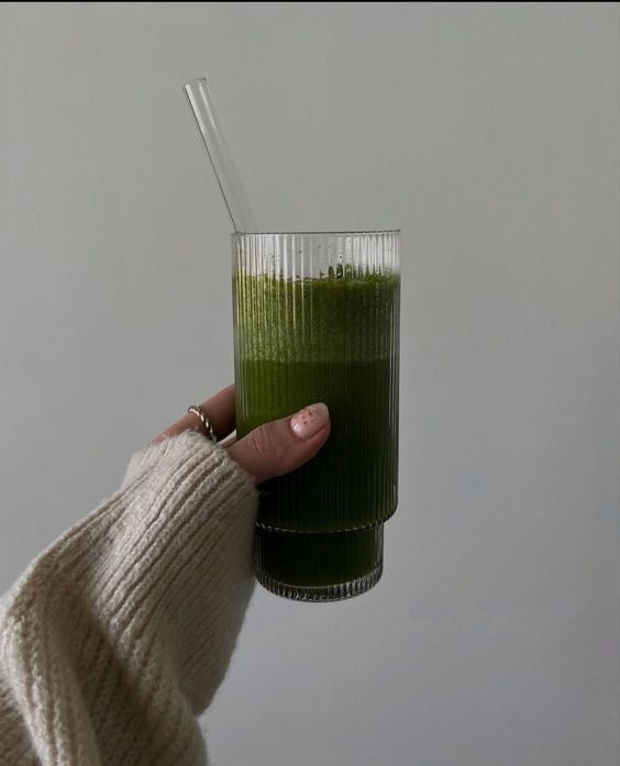 Elegant hand holding a glass of GRNS greens drink, showcasing a nutrient-rich blend with a smooth, vibrant green texture against a minimalist background