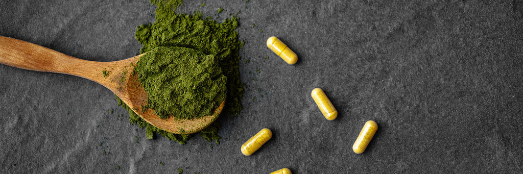 Close-up of green powder on a wooden spoon and golden capsules on a dark stone surface, showcasing natural supplements for health and wellness