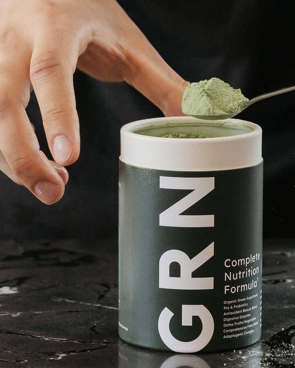 A tub of greens powder being scooped showing the greens powder inside