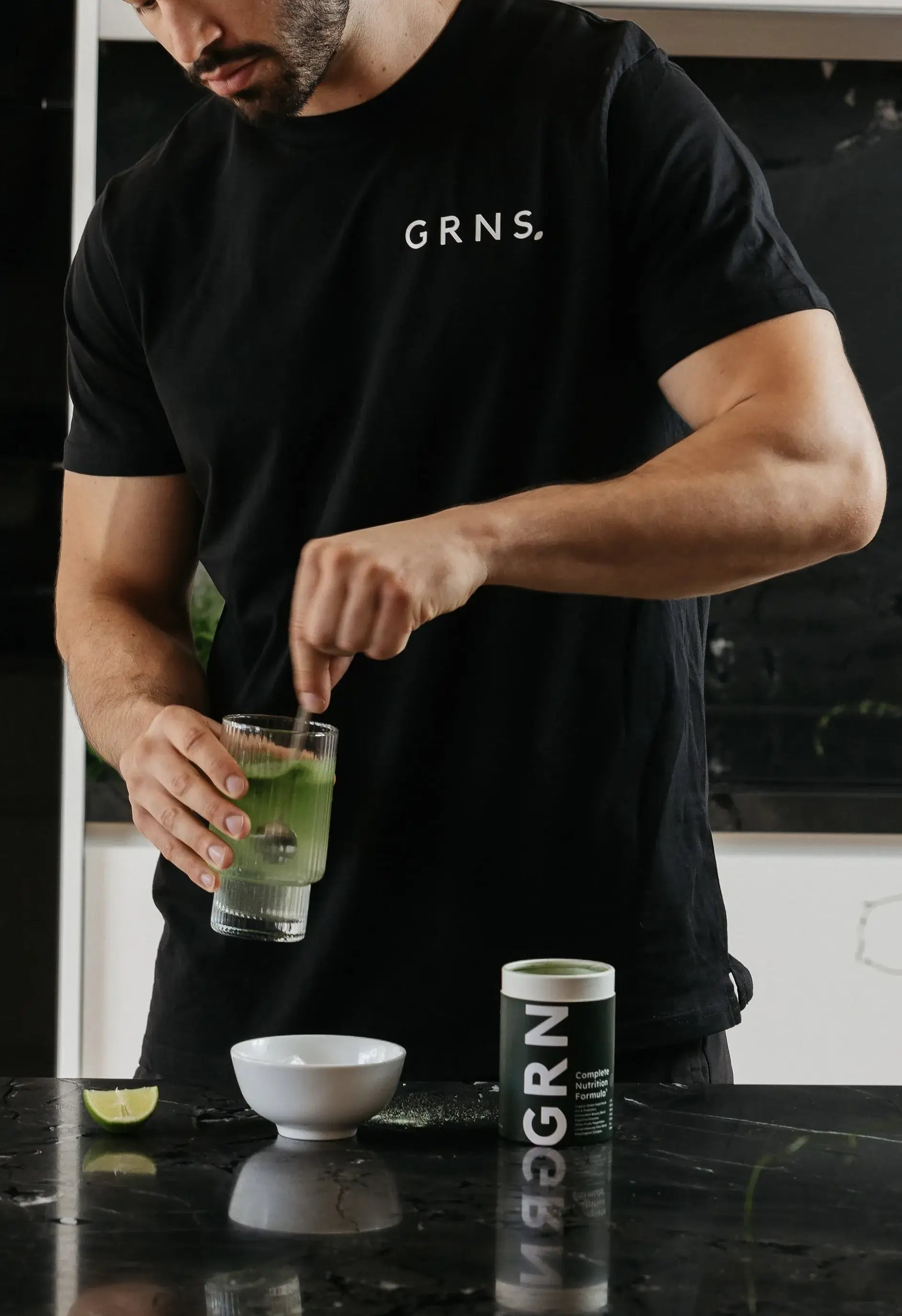 An athletic man mixing greens into a glass of water in an aesthetic kitchen
