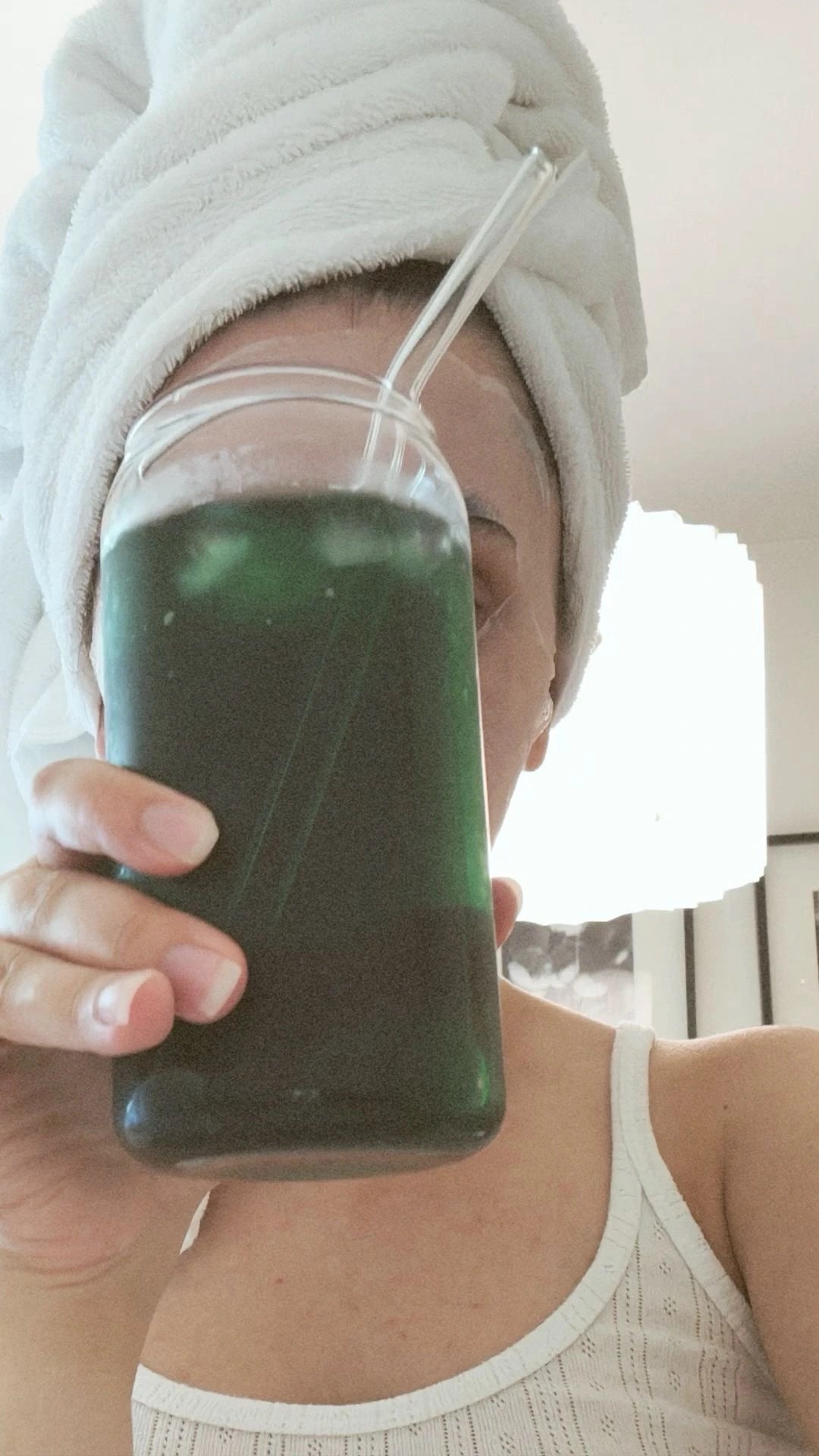 Close-up of a vibrant green drink with ice cubes in a clear glass, illuminated by natural sunlight, emphasising freshness and vitality